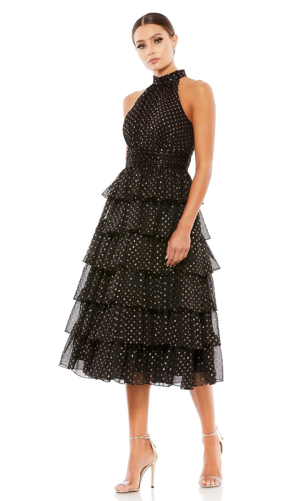 A woman in the Mac Duggal 49510 Midi Black Wedding-Guest Dress with gold polka dots and nude high heels stands against a white background.